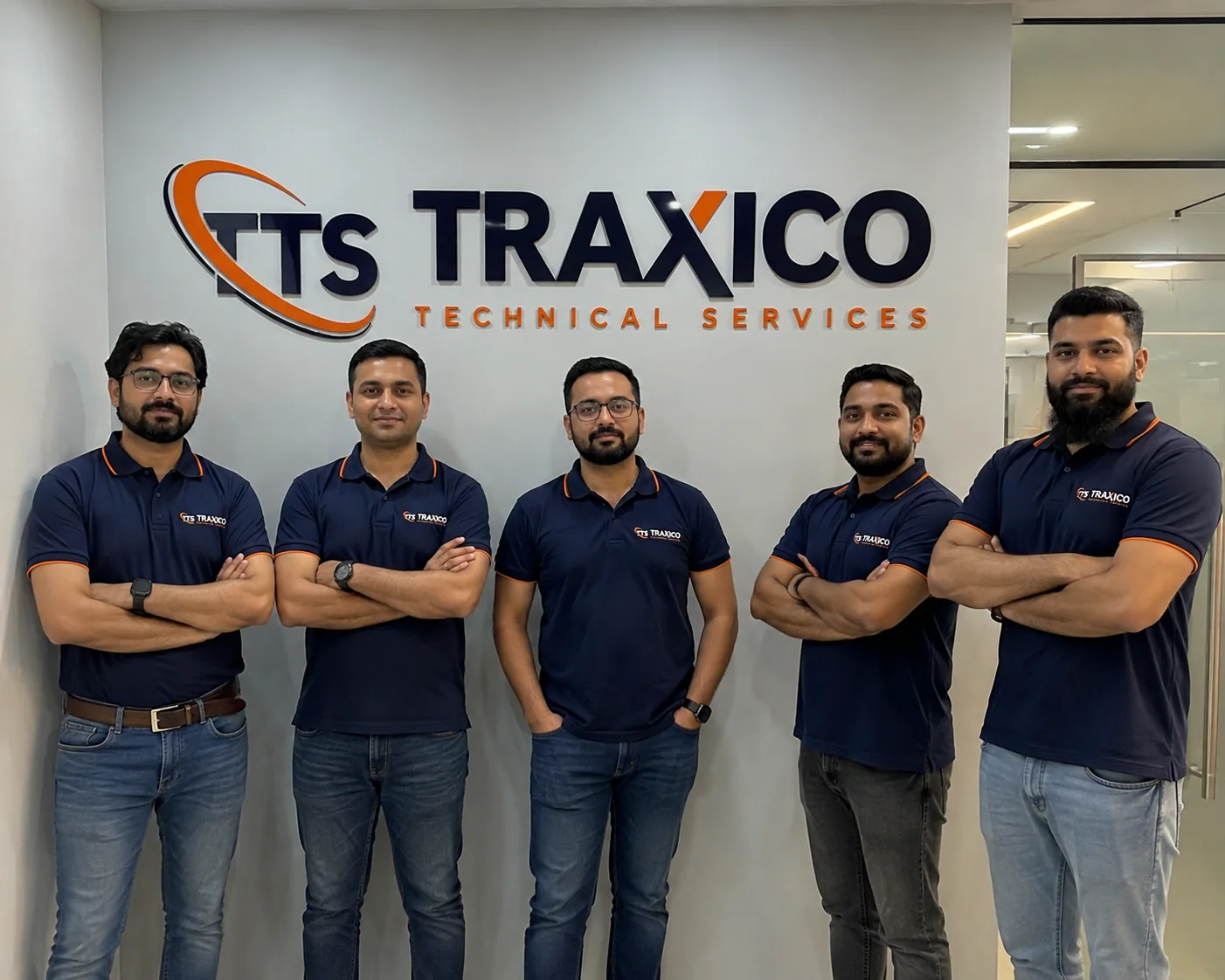 Five TRAXICO technicians in branded navy polo shirts standing in front of the company sign at the Dubai office